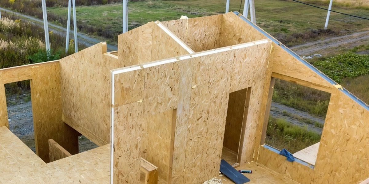 Casa moderna en construcción con diseño modular y revestimiento oscuro, vista lateral con cielo despejado y cierre perimetral de madera.